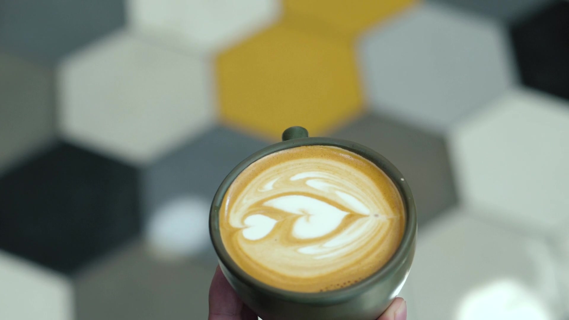 Un cappuccino con la rosetta disegnata nella schiuma, appoggiato sul pavimento a esagoni della caffetteria.